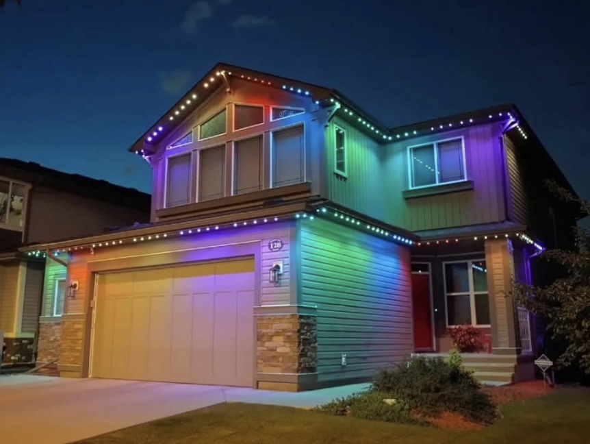 Two-story home washed in rainbow holiday colors after dark