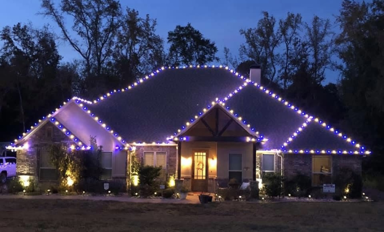 Stone home traced in purple and warm white holiday roofline lights
