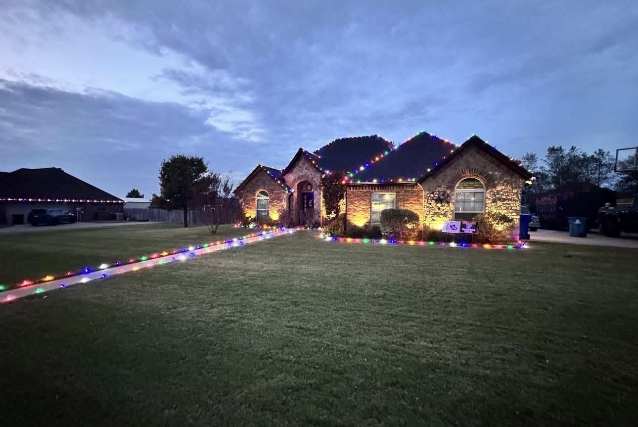 Brick home in multicolor holiday lights with a lit walkway at dusk