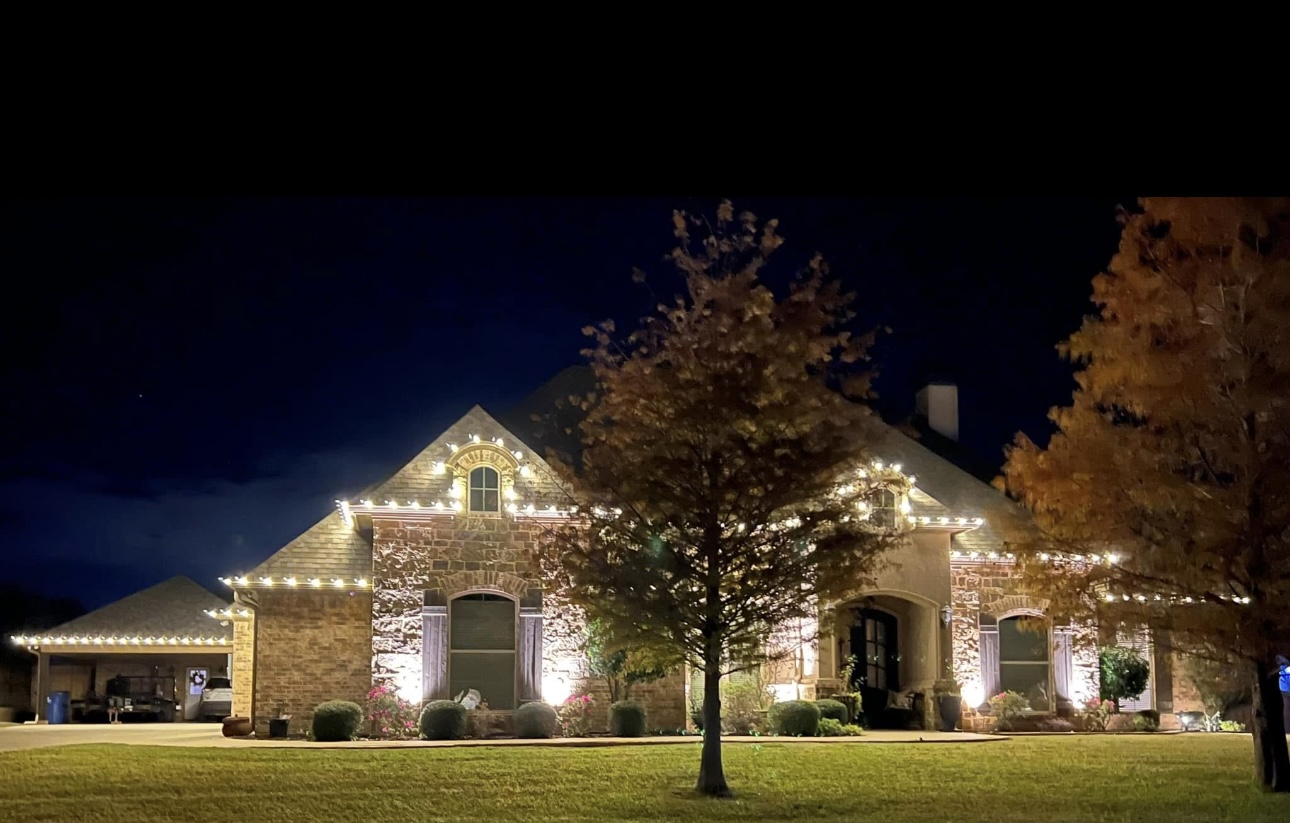 Stone home with warm white Christmas lights and uplit trees