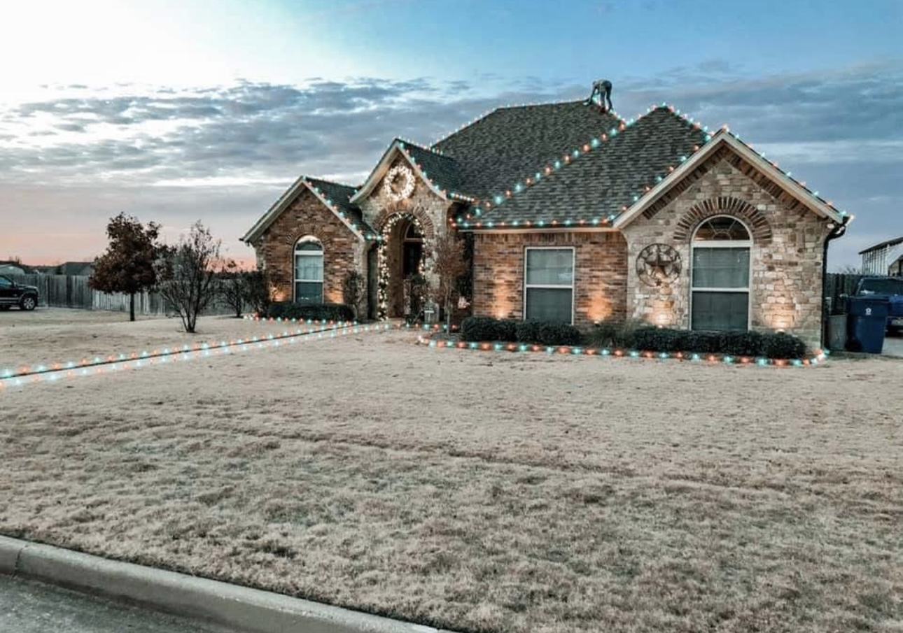 Stone home with red and teal holiday lights along the roofline and walkway